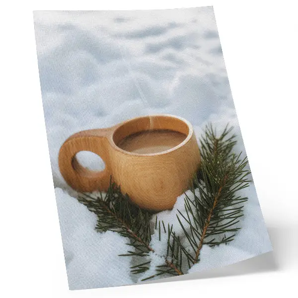 Decorative poster with a snowy landscape and green twigs on a wooden mug