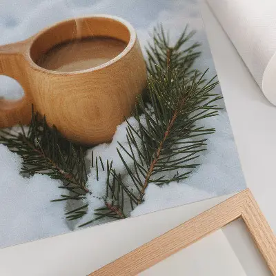 Decorative poster with a snowy landscape and green twigs on a wooden mug