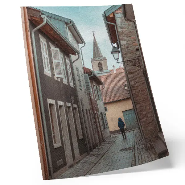 Poster narrow street with tenement houses and a tower with a blue coat
