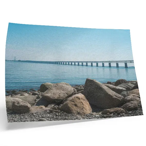 Decorative canvas print bridge over blue water with stones on the shore