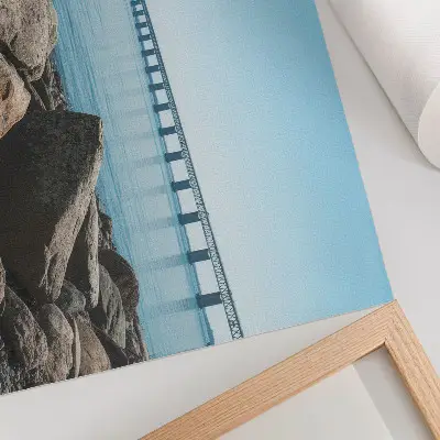 Decorative canvas print bridge over blue water with stones on the shore